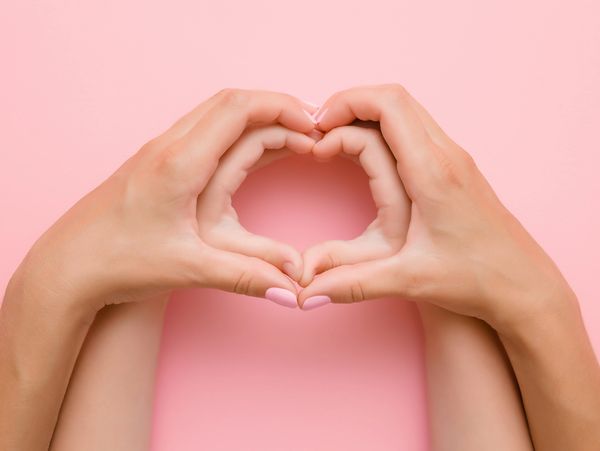 Hands forming a heart shape against a pink background.