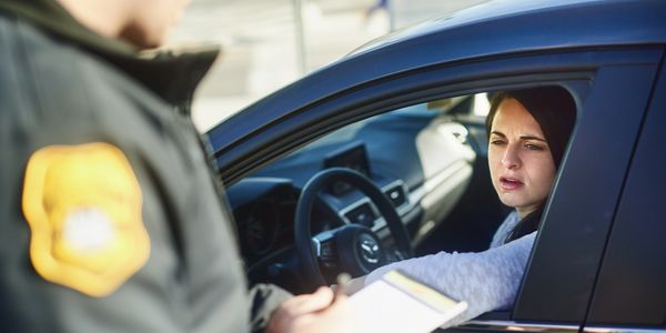 A woman in a car talking to a police officer with a ticket pad.