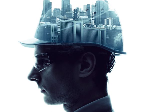 man wearing safety glasses and hardhat. Hardhat has buildings on it.