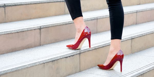 Woman wearing red high heels walking up stone stairs.