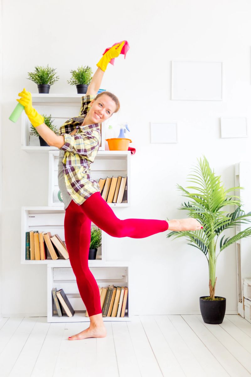 Woman in protective gloves is smiling and wiping dust using a spray and a duster while cleaning her house, close-up