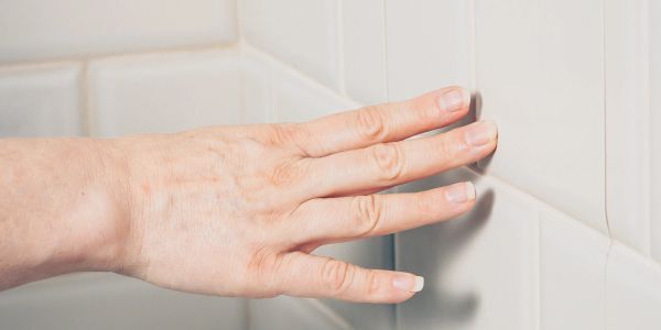 Hand touching white bathroom tiles.