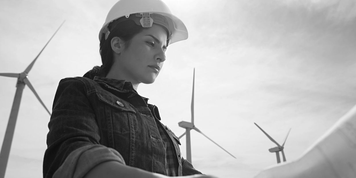 Woman engineer wearing a hard hat inspects wind turbines outdoors.
