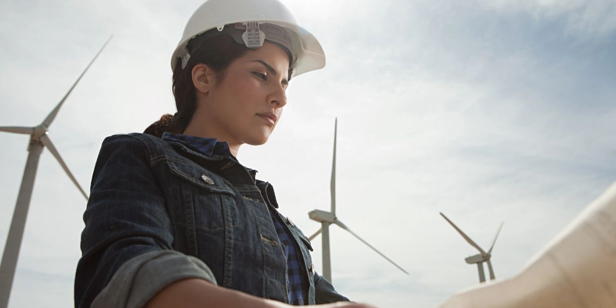 Woman engineer wearing a hard hat inspects wind turbines outdoors.