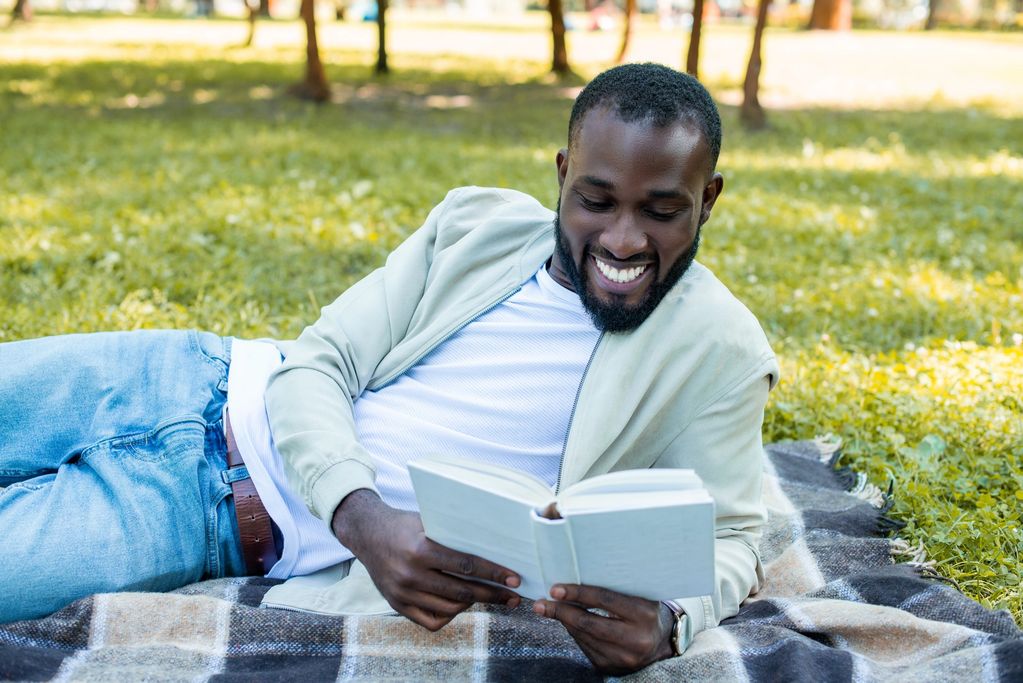 Man lying on grass reading a book and smiling.
