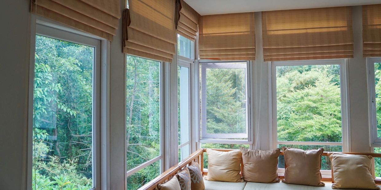 Cozy corner sofa with beige cushions by large windows overlooking lush greenery.