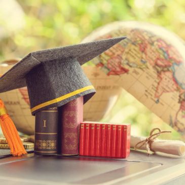 Graduation cap on books with a globe and diploma in the background.