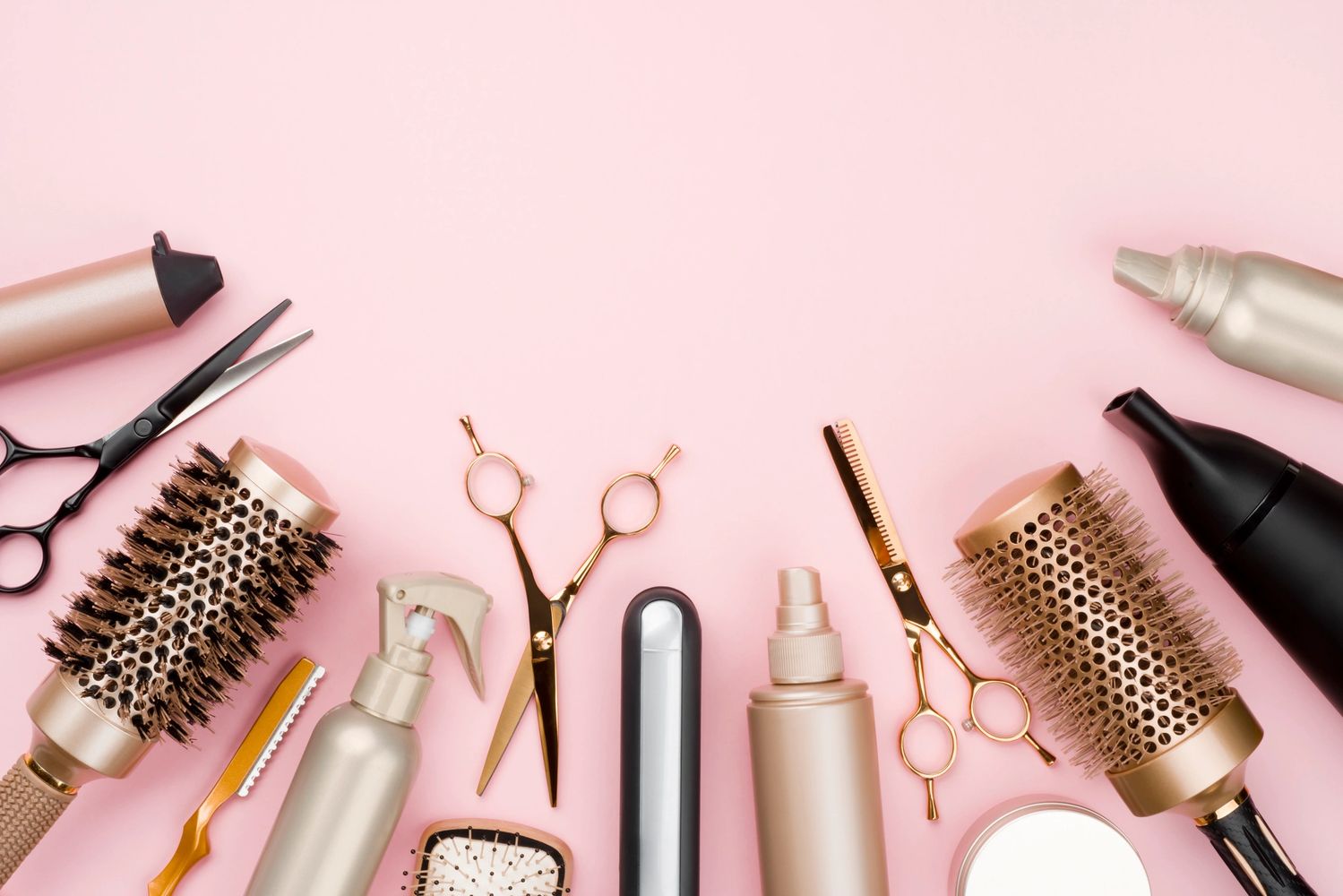 Hair styling tools and products arranged on a pink background.
