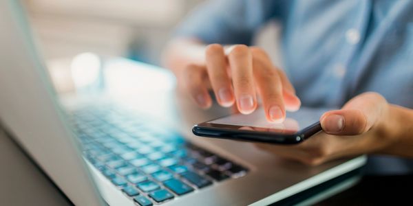 Person using a smartphone while working on a laptop.