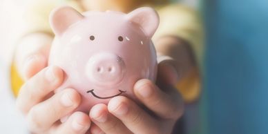 Hands holding a smiling pink piggy bank.