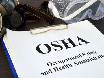 OSHA safety manual with protective goggles and respirator on a desk.