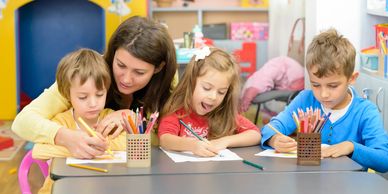 Teacher helps kids with coloring activities in a bright classroom.