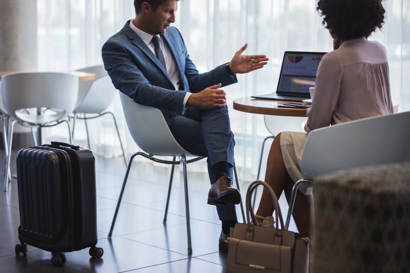 Business man showing something to woman while sitting at airport lounge. Business people working on laptop while waiting for their flight.