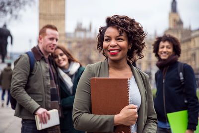 Smiling students holding notebooks with Big Ben in the background.