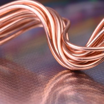 Close-up of twisted copper wires reflecting on a textured surface.