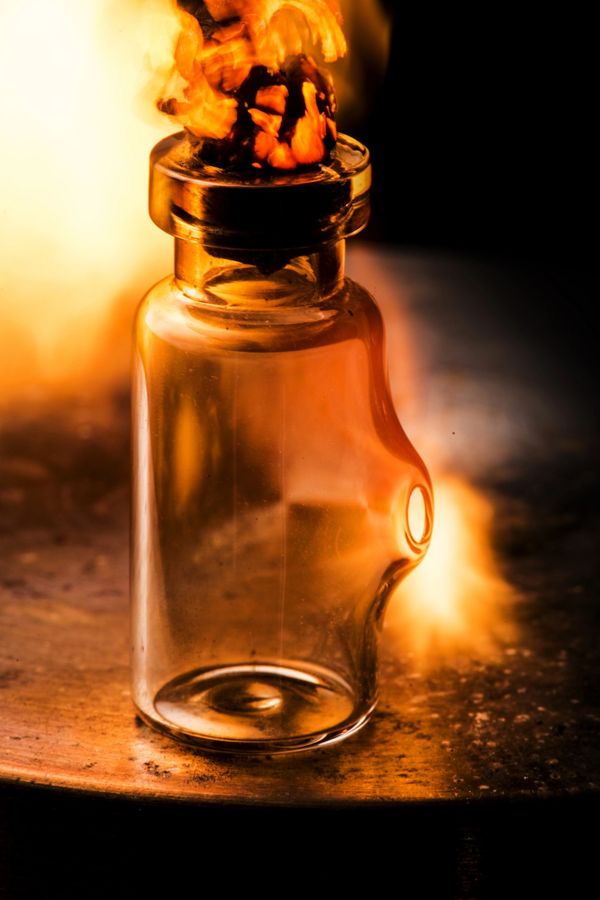 A glass bottle with a burning cork, glowing in warm firelight.