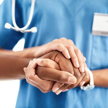 Healthcare worker comforting patient by holding their hand.