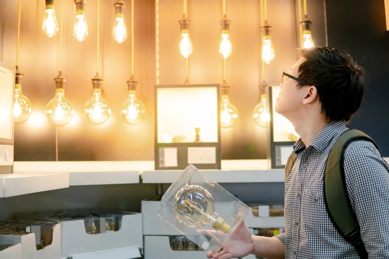 Young Asian man choosing package of electrical light bulb in the store. Furniture home decoration shopping concept