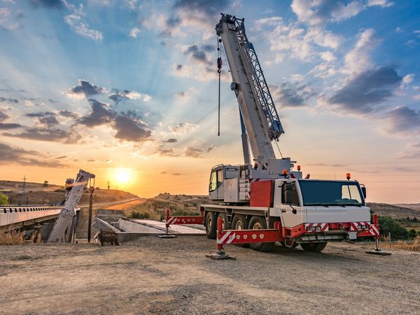 Mobile crane operating at a construction site during sunset.