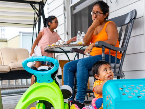A woman, two children, and colorful toys on a porch.
