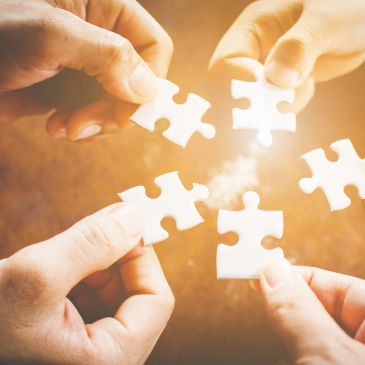 Four hands connecting white puzzle pieces.
