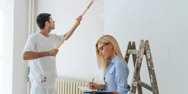 Man painting a wall while woman takes notes during home renovation.