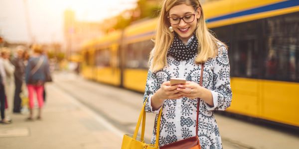 Woman in glasses smiling at her phone at a tram station.
