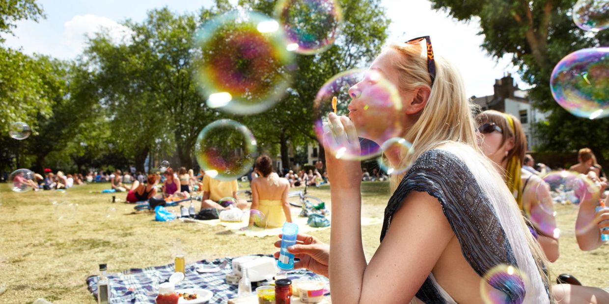 Woman blowing bubbles at a sunny park picnic.