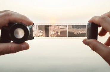 Hands holding a film strip with a magnifier against a bright background.