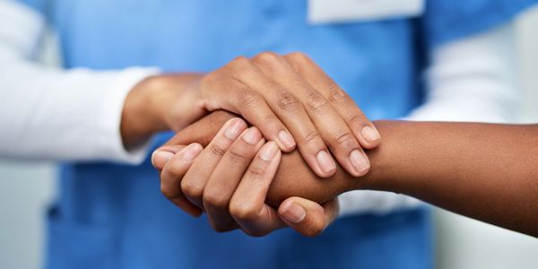 A healthcare worker comforting a patient with a supportive hand grasp.