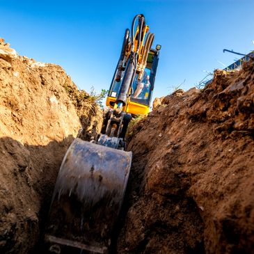 Excavator digging a deep trench under clear blue sky.