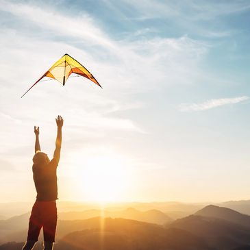 Person flying a yellow kite at sunset over hills.