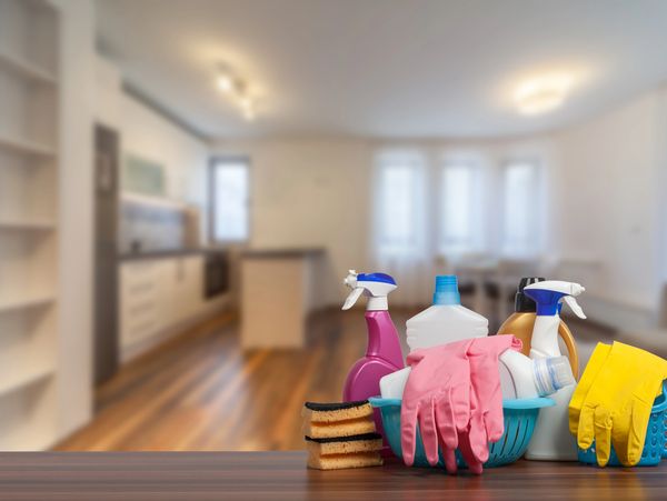 Cleaning supplies and gloves on a table with a blurred kitchen background.