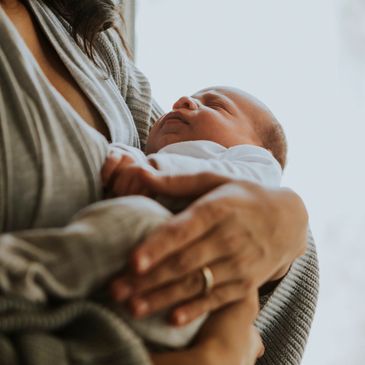 A person gently cradles a sleeping newborn baby in their arms.