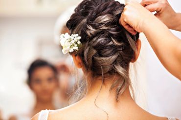 A woman getting her braided hair styled with white flowers.