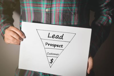 Person holding a sales funnel diagram with stages Lead, Prospect, Customer, and revenue symbol.