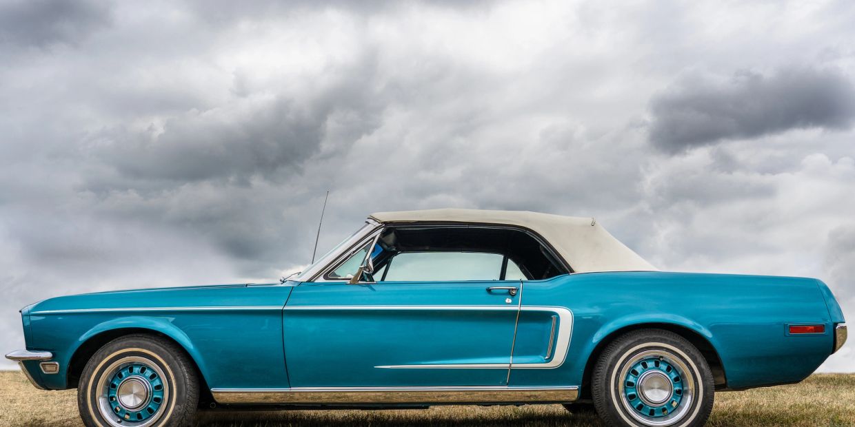 Classic blue convertible car parked on grass under cloudy sky.