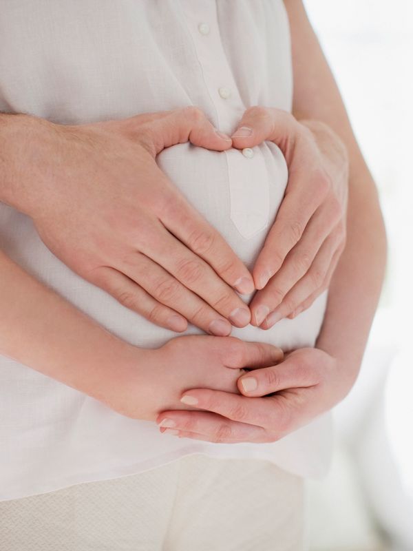 A loving couple forms a heart shape with their hands on a pregnant belly, symbolizing care and connection. The image reflects the supportive presence of doula services and the holistic wellness journey that nurtures both mother and baby.