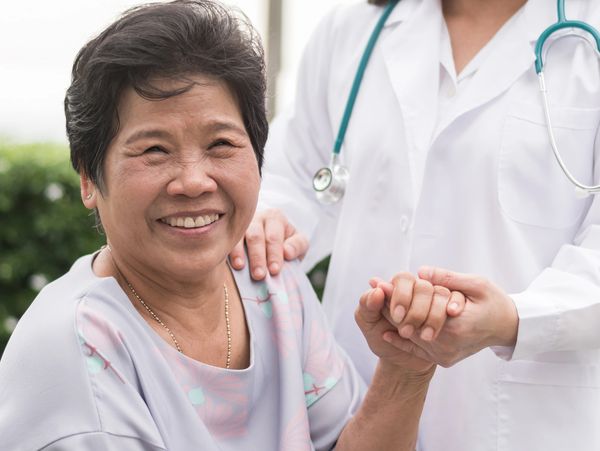 Smiling elderly woman holding hands with a doctor in a supportive gesture.