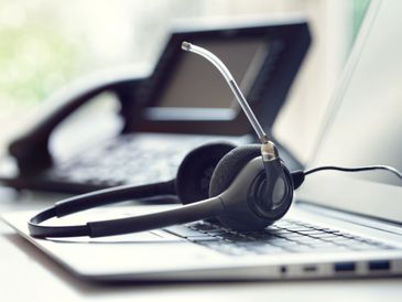 A headset resting on a laptop keyboard with a blurred phone in the background.