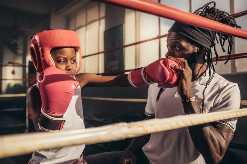 Kid practicing punches wearing boxing gloves and headgear with his coach. Boxing coach teaching the techniques of punching to a kid.