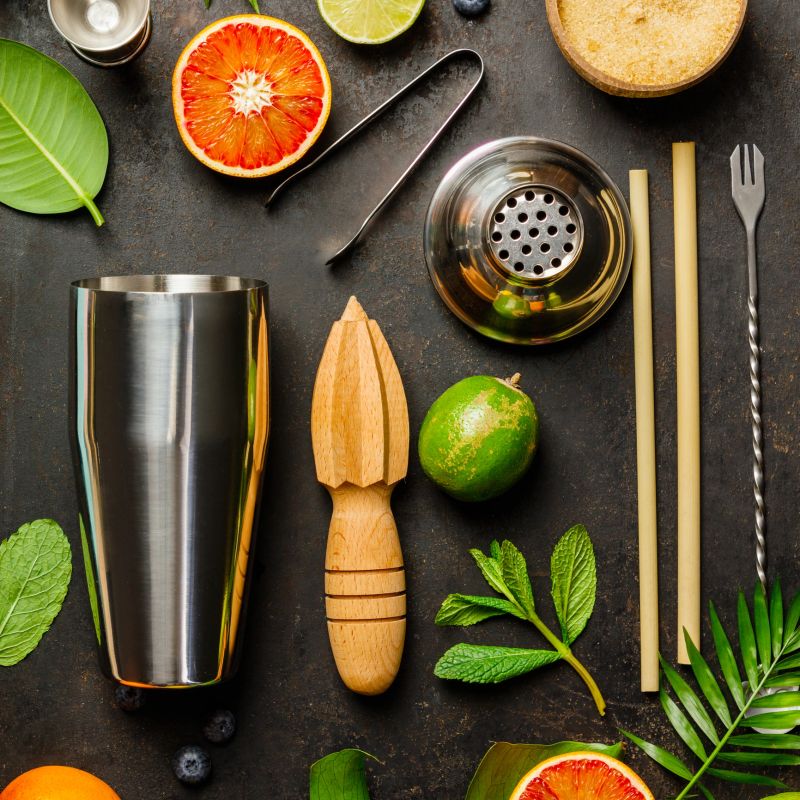 Cocktail making bar tools, shaker, tropical fruits and leaves on a dark background. Top view