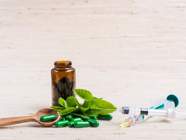 Green capsules, syringe, and leaves on a beige surface.