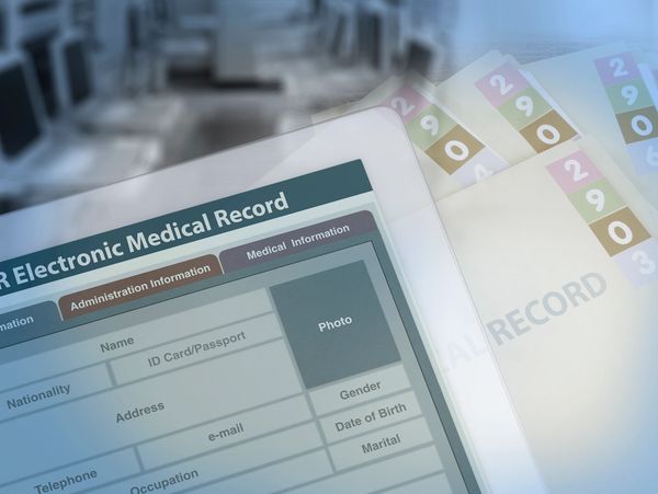 Digital electronic medical record displayed on a tablet with patient file folders in the background.