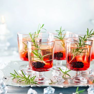 Glasses of red cocktail with rosemary and berries.