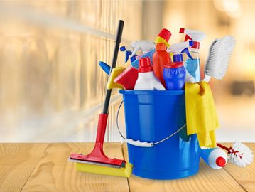 Blue bucket filled with assorted cleaning supplies and tools on a wooden surface.