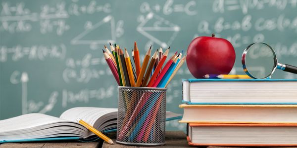 School supplies including colored pencils, books, an apple, and a magnifying glass on a desk.