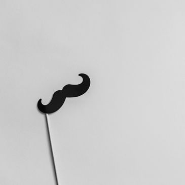 Black mustache on a stick against a beige background.
