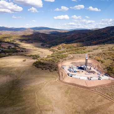 A drilling rig setup in a valley surrounded by hills under a blue sky.