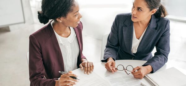 Two professional women discussing documents in an office setting.